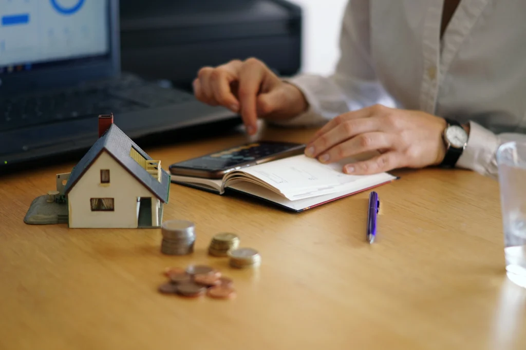 Persona escribiendo con una casita y algunas monedas